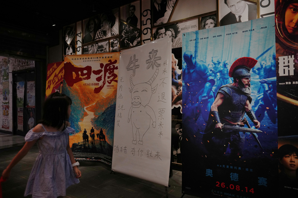 A child looks at a drawing poster promoting a Chinese animated film "Niu Lai" on display with other movie posters at a cinema in Beijing, Tuesday, Aug. 18, 2026. (AP Photo/Andy Wong)