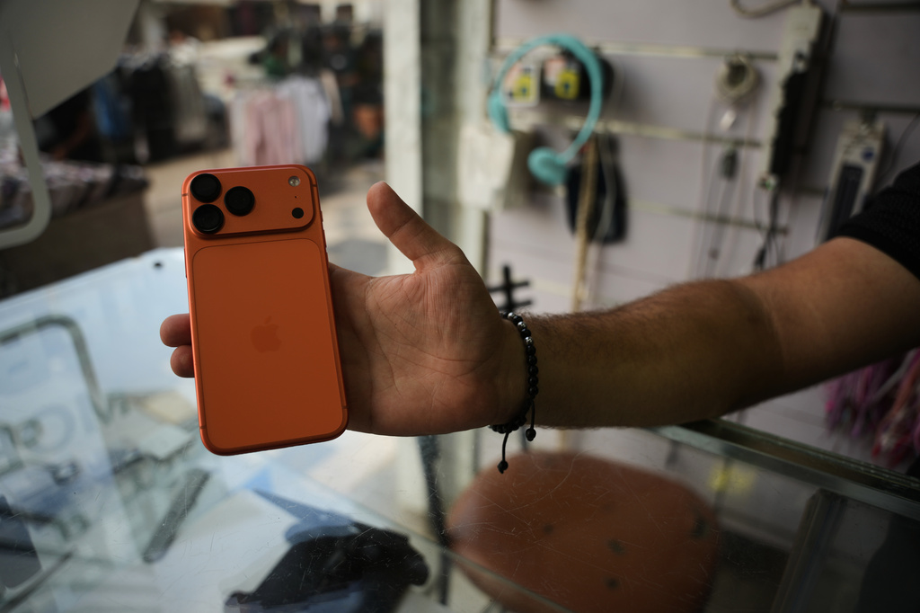 A Palestinian salesman shows an iPhone 17 Pro Max to the camera at a mobile phone store in Gaza City, Sunday, Aug. 16, 2026. (AP Photo/Abdel Kareem Hana)