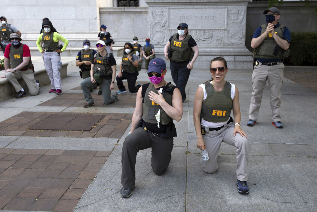 FILE - Federal Bureau of Investigation (FBI) officers take a knee with demonstrators, as they march on Pennsylvania Ave, June 4, 2020, in Washington, during a protest over the death of George Floyd, an unarmed black man, who died after a police officer kneeled on his neck for several minutes. (AP Photo/Jose Luis Magana, File)