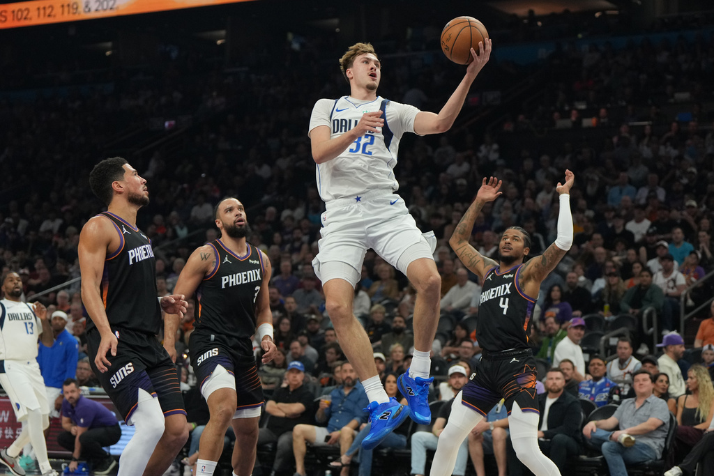 Dallas Mavericks forward Cooper Flagg scores between Phoenix Suns guard Devin Booker, forward Dillon Brooks (3), and guard Jalen Green (4) during the first half of an NBA basketball game, Tuesday, Feb. 10, 2026, in Phoenix. (AP Photo/Rick Scuteri)