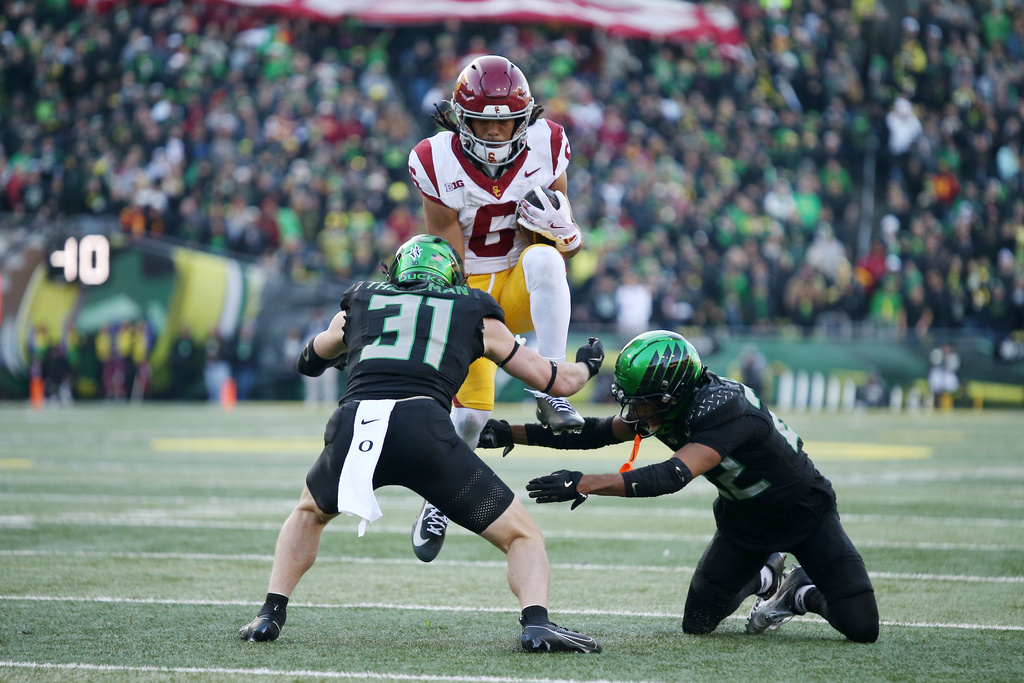 Southern California wide receiver Makai Lemon (6) attempts to hurdle Oregon defensive backs Dillon Thieneman (31) and Jadon Canady, right, during the first half of an NCAA college football game Saturday, Nov. 22, 2025, in Eugene, Ore. (AP Photo/Lydia Ely)