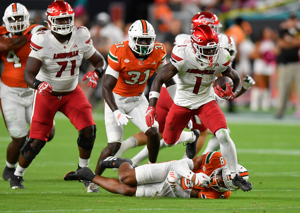 Louisville running back Isaac Brown (1) runs over Miami defensive back Jakobe Thomas (8) during the first half of an NCAA college football game, Friday, Oct. 17, 2025, in Miami Gardens, Fla. (AP Photo/Michael Laughlin)