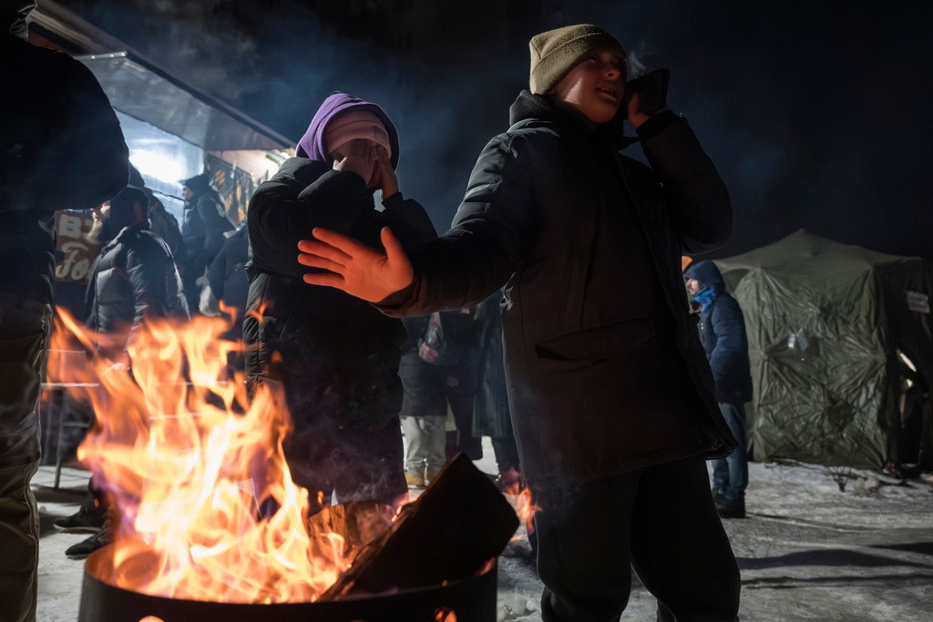 People warm up at the fire as veterans of the 3rd Separate Assault Brigade of Ukraine's Armed Forces serve free hot meals in a residential neighborhood for people without power in their homes in Kyiv, Ukraine, Saturday, Jan. 31, 2026.(AP Photo/Vladyslav Musiienko)