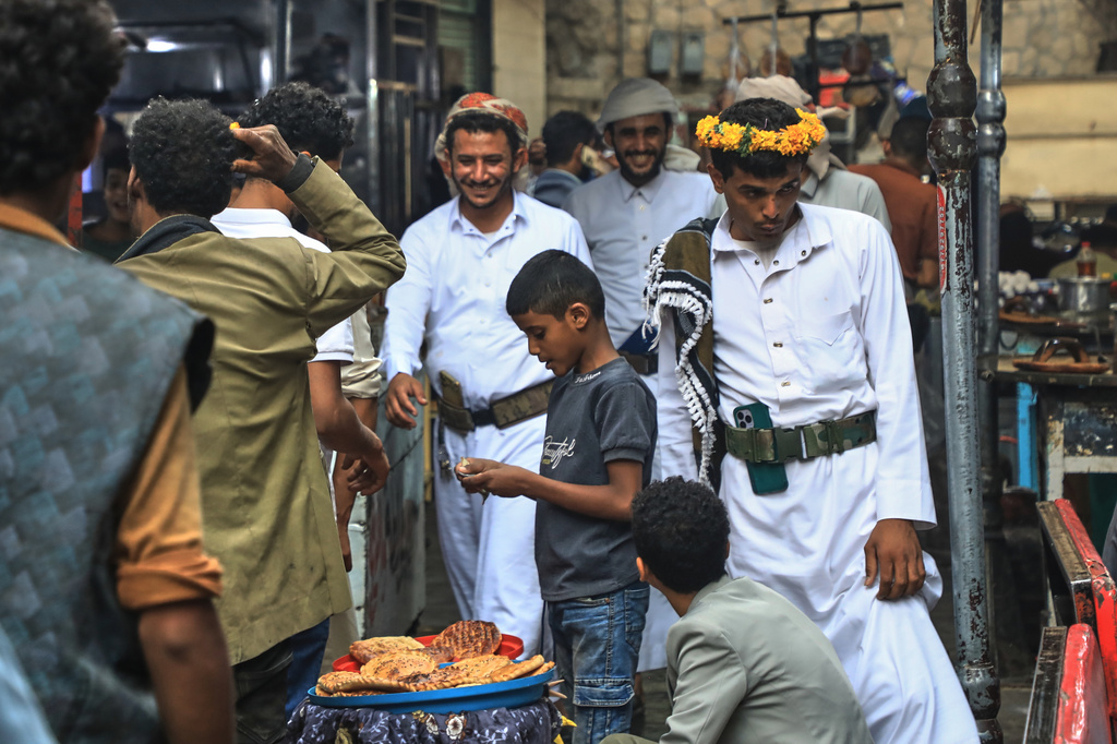 People walk past a boy selling bread at a street market in Sanaa, Yemen, Saturday, Aug. 8, 2026. (AP Photo/Osamah Abdulrahman)