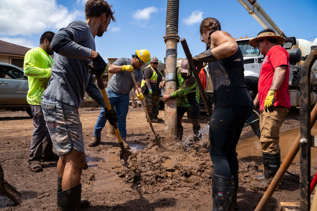 Volunteers shovel mud and debris from a flooded residential neighborhood, Tuesday, March 24, 2026, in Waialua, Hawaii. (AP Photo/Mengshin Lin)