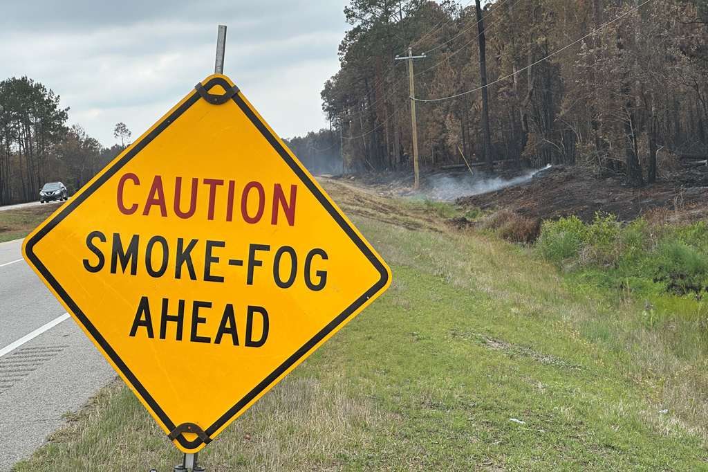 Blackened trees and charred palmetto fronds lined the shoulders of U.S. 82 on Monday, April 27, 2026 in Brantley County, Ga., as smoke poured from the ground in several spots beside the highway. (AP Photo/Russ Bynum)