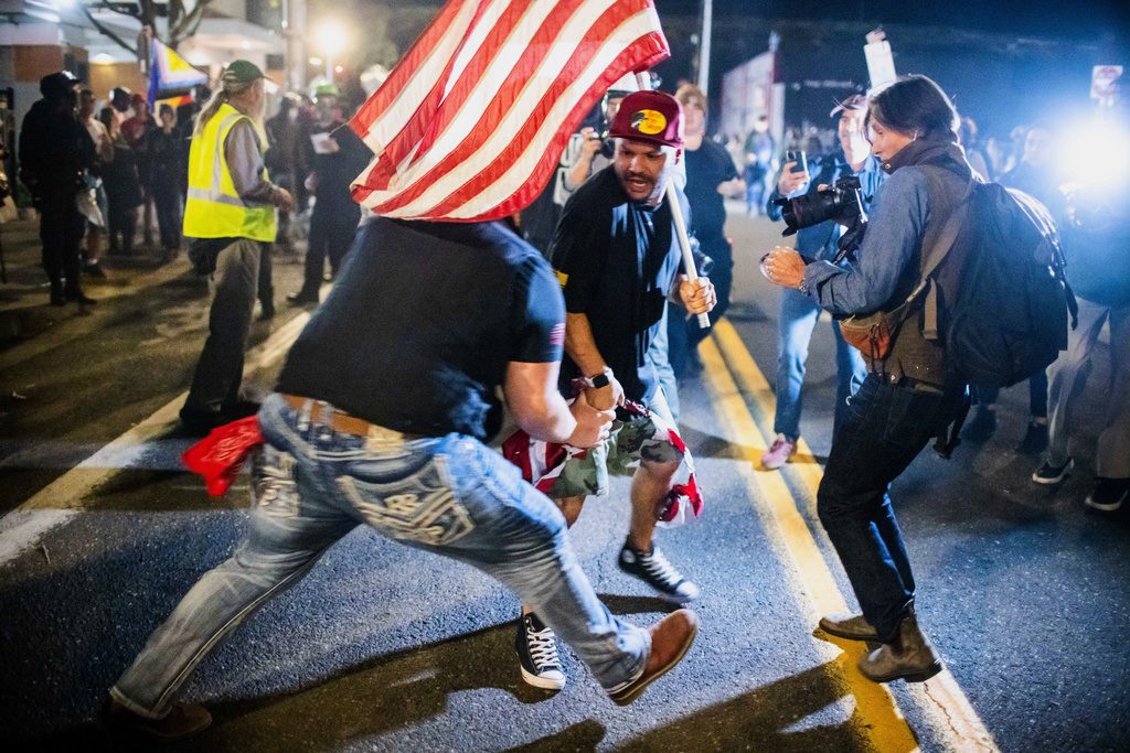 A Trump supporter, center, scuffles with a protester over a burning U.S. flag during a protest outside a U.S. Immigration and Customs Enforcement facility in Portland, Ore., Monday, Oct. 6, 2025. (AP Photo/Ethan Swope)