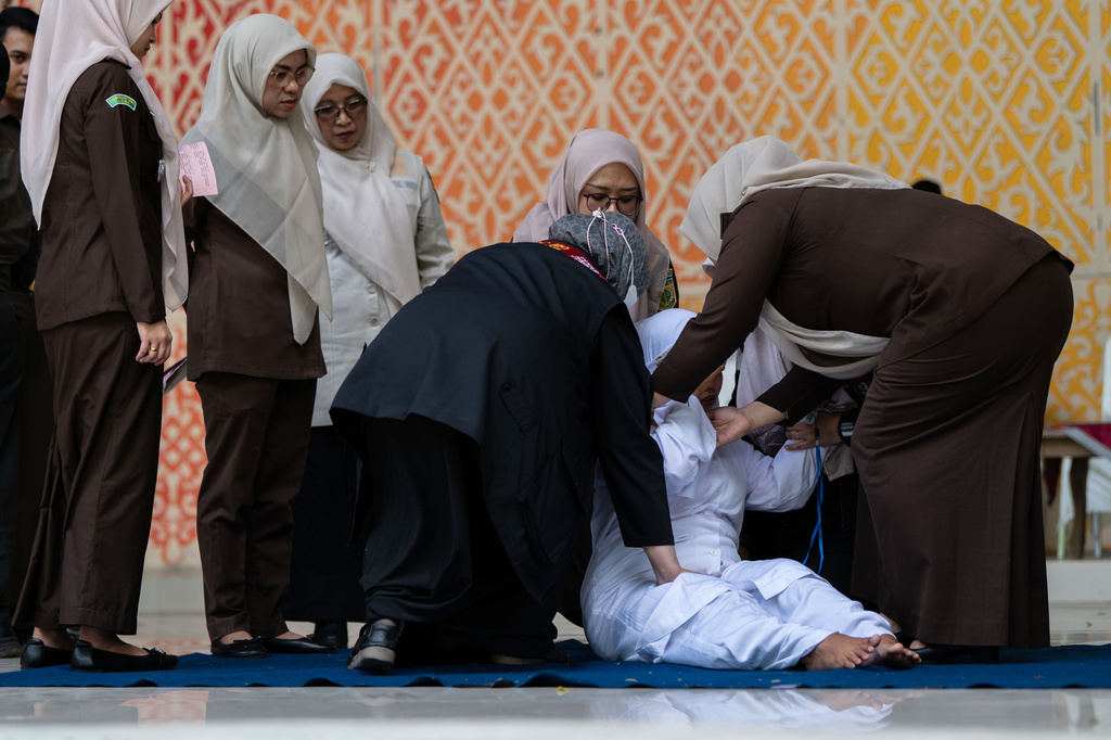 Shariah law officials assist an unmarried woman, convicted of violating Islamic law by kissing during a TikTok livestream, to get up after being being publicly caned, in Banda Aceh, Indonesia, Thursday, July 2, 2026. (AP Photo/Reza Saifullah)