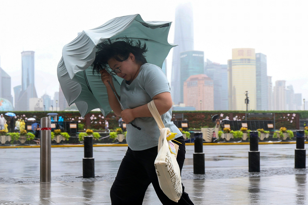In this photo released by Xinhua News Agency, a woman struggles with her umbrella in strong wind and rain ahead of Typhoon Dolphin at Huangpu District of Shanghai on Sunday, Aug. 9, 2026.(Wang Xiang/Xinhua via AP)