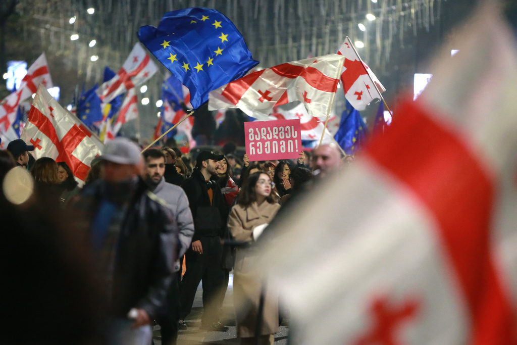 Demonstrators with Georgian and EU flags gather in the Georgian capital of Tbilisi, on Friday, Nov. 28, 2025, to mark 365 days of non-stop protests against the government's decision to halt talks on joining the European Union. The banner center reads: regime must resign. (AP Photo/Zurab Tsertsvadze)