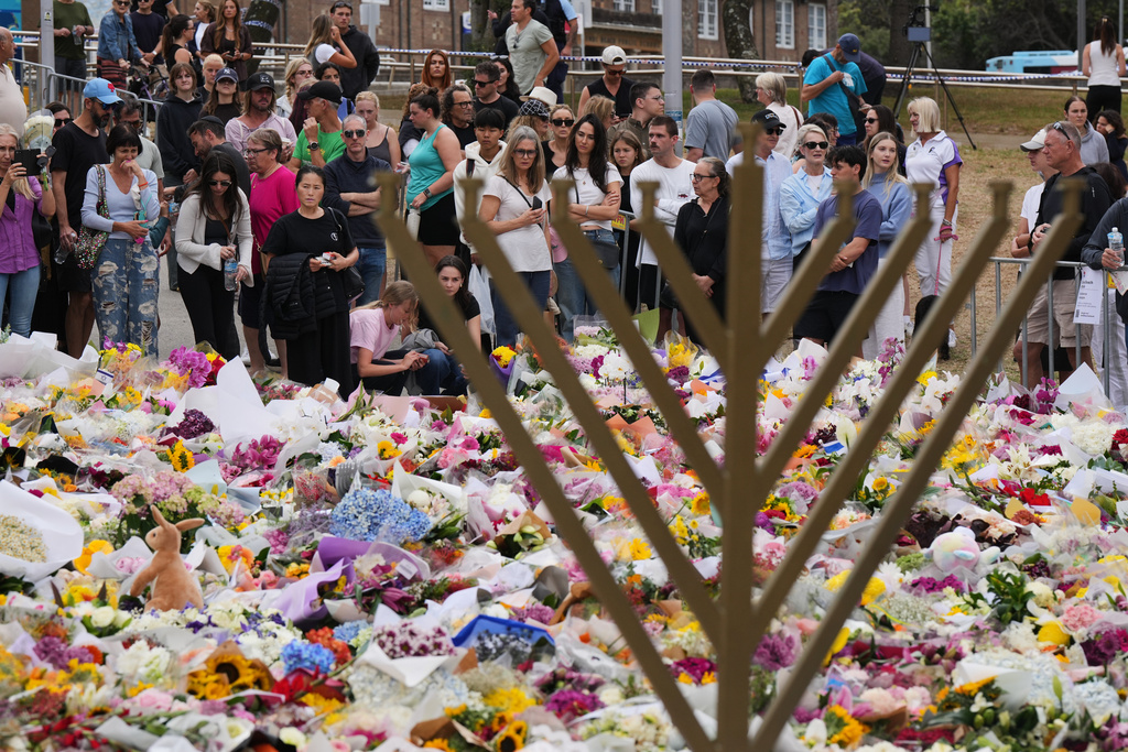 A Hanukkah menorah stands by a floral tribute as people gather to pay their respects near the Bondi Pavilion at Bondi Beach on Tuesday, Dec. 16, 2025, following Sunday's shooting in Sydney, Australia. (AP Photo/Mark Baker)