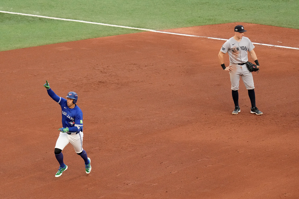Toronto Blue Jays designated hitter George Springer, left, celebrates as he rounds the bases following his solo home run as New York Yankees first baseman Ben Rice, right, looks on during the fifth inning of Game 2 of baseball's American League Division Series in Toronto, Sunday, Oct. 5, 2025. (Chris Young/The Canadian Press via AP)