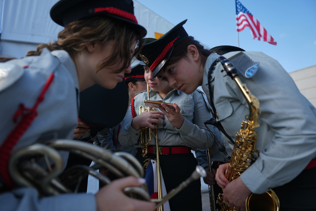 Members of an Israeli military band listen to a live broadcast showing the first group of hostages being released from Hamas captivity in Gaza, ahead of a welcoming ceremony for U.S. President Donald Trump's arrival at Ben Gurion Airport near Tel Aviv, Israel, Monday, Oct. 13, 2025. (AP Photo/Ariel Schalit)