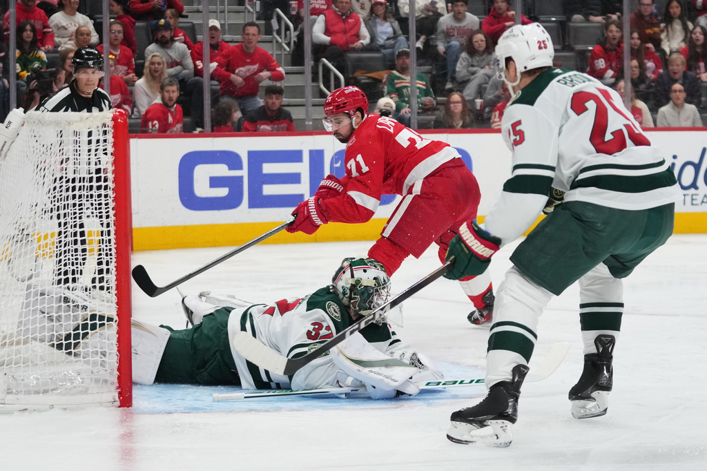 Detroit Red Wings center Dylan Larkin (71) shoots but misses as Minnesota Wild goaltender Filip Gustavsson (32) defends and defenseman Jonas Brodin (25) looks on in the second period of an NHL hockey game Sunday, April 5, 2026, in Detroit. (AP Photo/Paul Sancya)