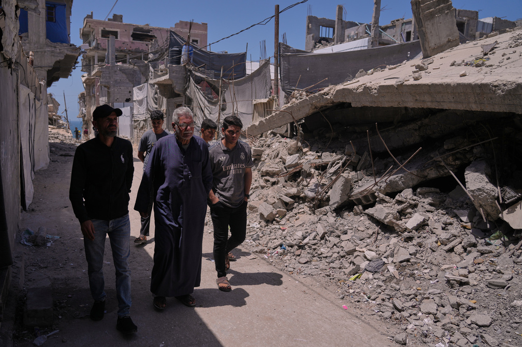 Palestinian Yusuf Abu Hamam, front center, who was expelled from his town during the first Israeli-Arab war in 1948, walks with his grandchildren and son past buildings destroyed during Israeli air and ground operations in the Shati refugee camp in Gaza City, Wednesday, May 13, 2026. (AP Photo/Jehad Alshrafi)