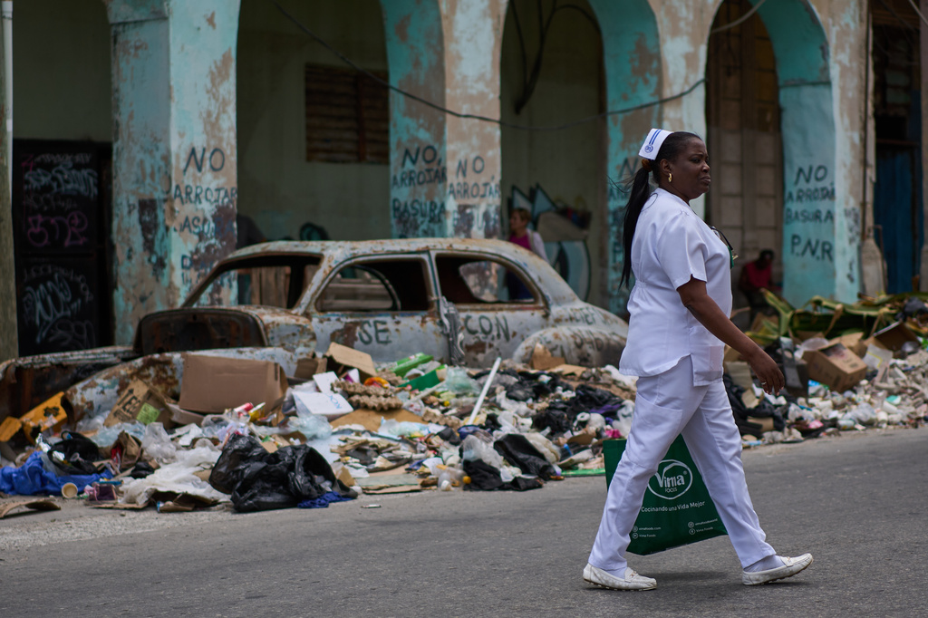 A nurse walks past trash and an abandoned classic American car on a street in Havana, Wednesday, April 22, 2026. (AP Photo/Ramon Espinosa)