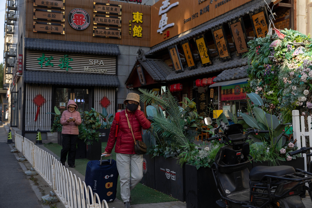 A woman pulls her luggage past a building known for its Japanese restaurants in Beijing, on Nov. 24, 2025. (AP Photo/Ng Han Guan)