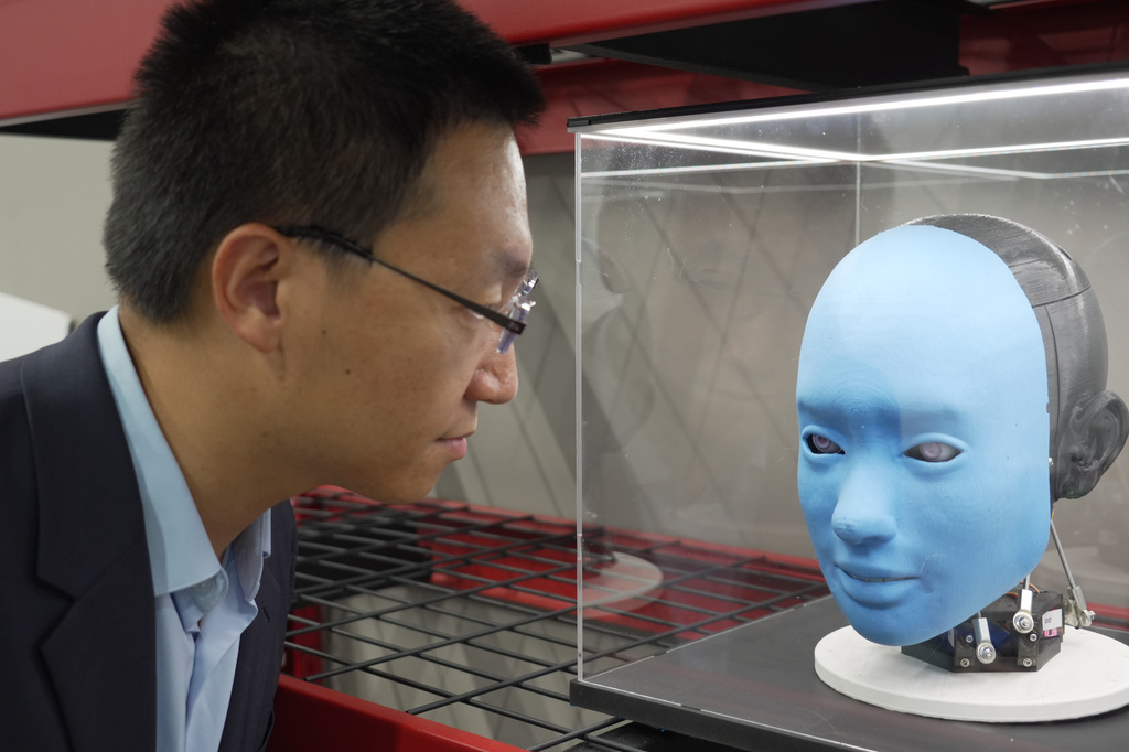 Professor Boyuan Chen is reflected in a glass case as he looks at a humanoid robot at Duke University's General Robotics Lab in Durham, N.C., Tuesday, May 26, 2026. (AP Photo/Allen G. Breed)