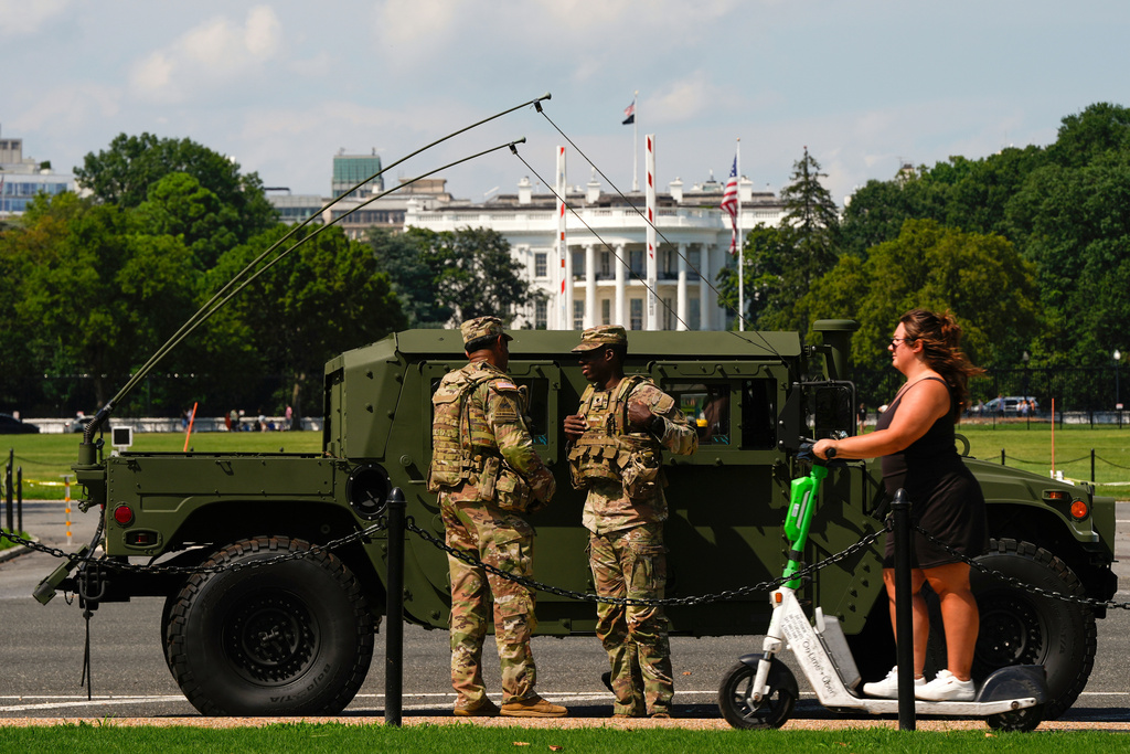 Members of the District of Columbia National Guard patrol in front of the White House as a woman rides past on a scooter, Saturday, Aug. 16, 2025, in Washington. (AP Photo/Julia Demaree Nikhinson)