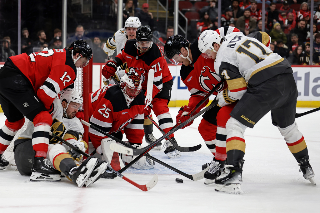 New Jersey Devils goaltender Jacob Markstrom (25) defends his net against Vegas Golden Knights center Tomas Hertl, on ice, and defenseman Ben Hutton (17) during the first period of an NHL hockey game Friday, Dec. 5, 2025, in Newark, N.J. (AP Photo/Adam Hunger)