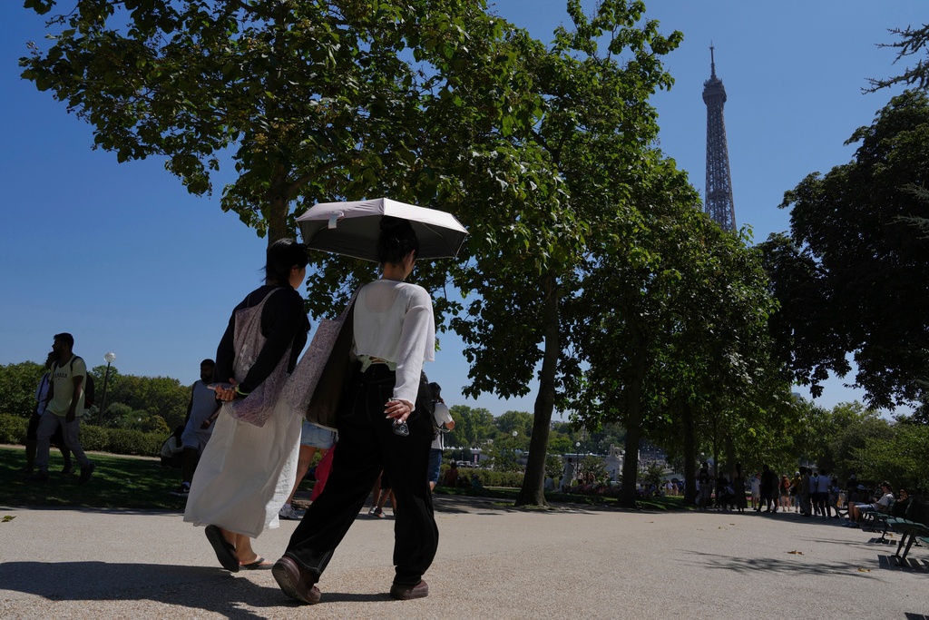 FILE - Tourists use an umbrella as they walk an alley of the Trocadero gardens during a hot day Monday, Aug. 11, 2025, in Paris. (AP Photo/Aurelien Morissard, File)
