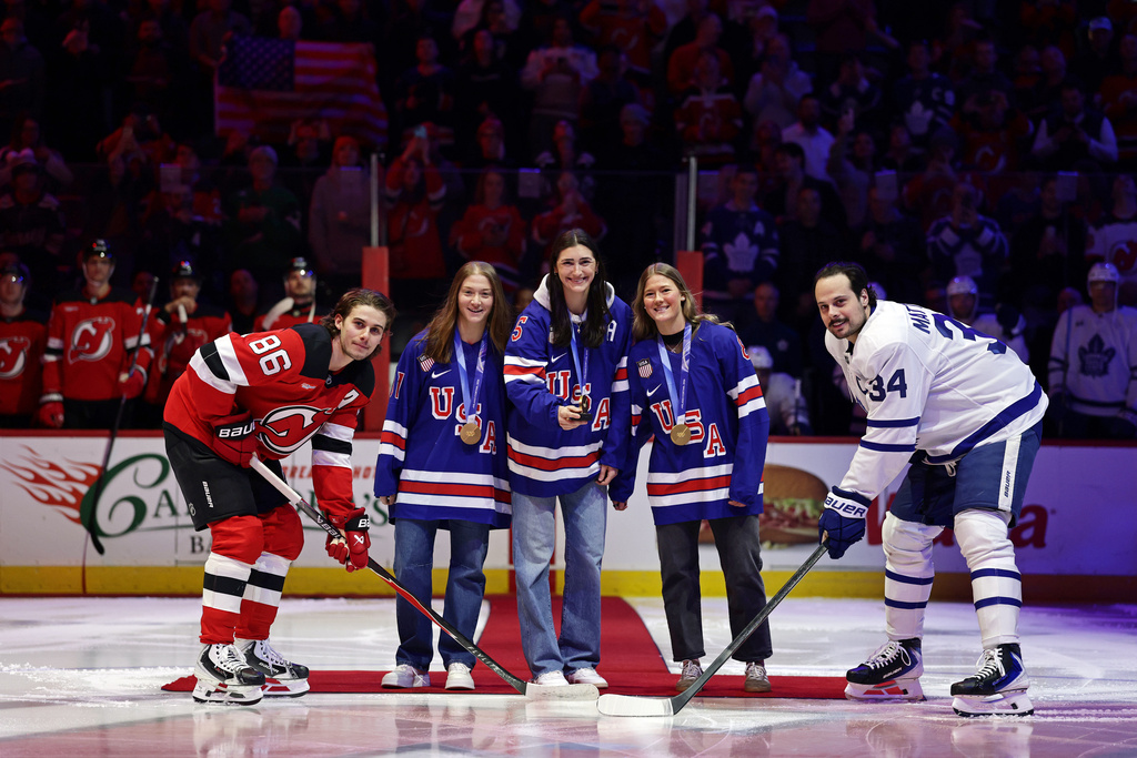 United States women's gold medal hockey players, center left to right, Aerin Frankel, Megan Keller and Haley Winn with New Jersey Devils center Jack Hughes (86) and Toronto Maple Leafs center Auston Matthews (34) for a ceremonial puck drop before an NHL hockey game Wednesday, March 4, 2026, in Newark, N.J. (AP Photo/Adam Hunger)