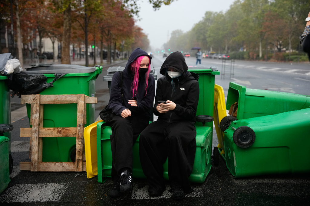 A student checks her smartphone in front of the Helene Boucher high school blockaded with garbage bins during a protest against under-resourced schools in Paris, Tuesday, Oct. 13, 2026. (AP Photo/Teresa Suarez)