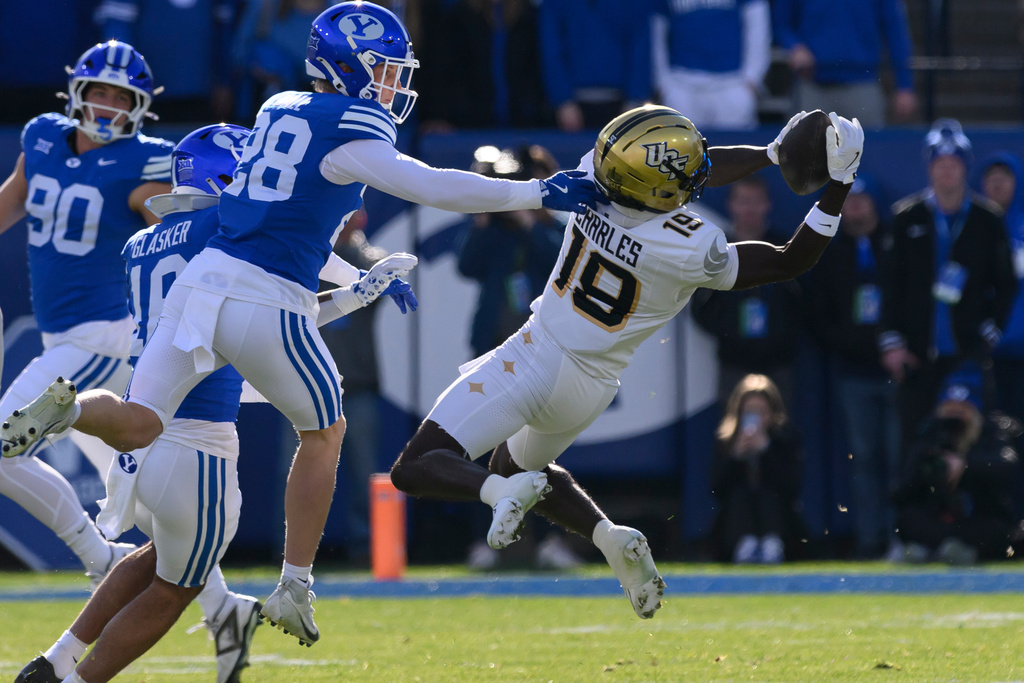 UCF wide receiver Waden Charles (19) rotates his body mid-air to make the catch defended by BYU safety Tanner Wall (28) during the first half an NCAA college football game, Saturday, Nov. 29, 2025, in Provo, Utah. (AP Photo/Tyler Tate)