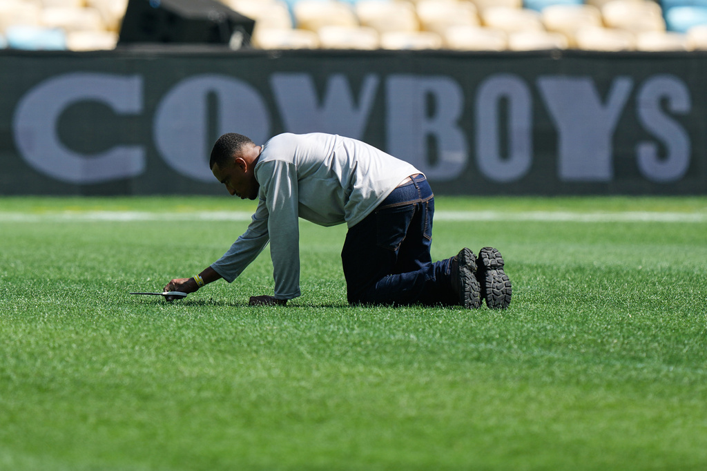 A worker cuts grass with scissors on the field ahead of an NFL football game between the Dallas Cowboys and the Baltimore Ravens in Rio de Janeiro, Saturday, Sept. 26, 2026. (AP Photo/Fernando Llano)
