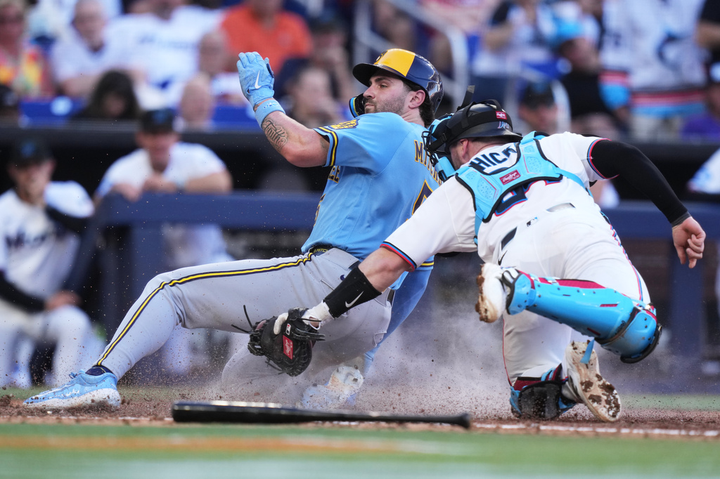 Milwaukee Brewers' Garrett Mitchell, left, beats the throw to Miami Marlins catcher Liam Hicks, right, to score during the sixth inning of a baseball game, Saturday, April 18, 2026, in Miami. (AP Photo/Lynne Sladky)