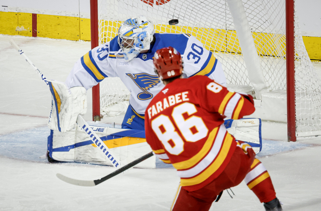 St. Louis Blues goalie Joel Hofer, left, lets in a goal from Calgary Flames' Joel Farabee that was later called back during second period NHL hockey action in Calgary on Wednesday, March 18, 2026. (Jeff McIntosh/The Canadian Press via AP)