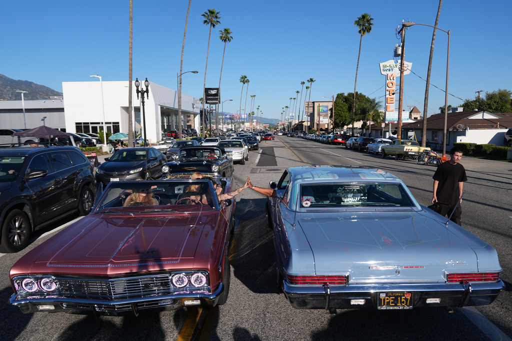 Sandy Avila, left, driving a 1966 Chevy Impala SS, high-fives a fellow lowrider at the 6th Annual Lady Lowrider Cruise Night in celebration of International Women's Day in Pasadena, Calif., on Sunday, March 8, 2026. (AP Photo/Damian Dovarganes)