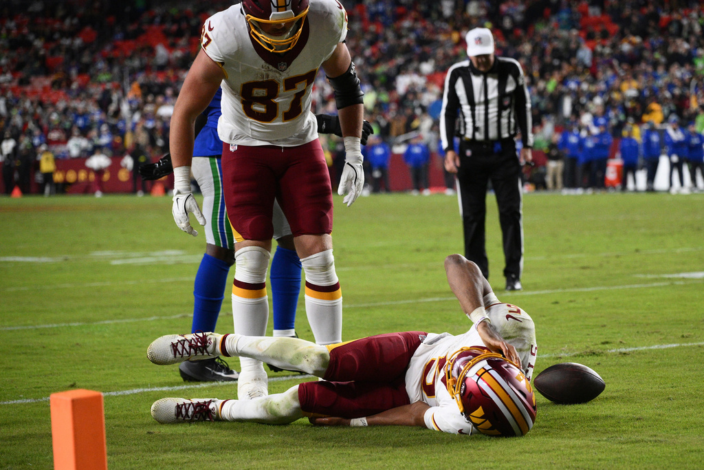 Washington Commanders tight end John Bates (87) looks over at his teammate quarterback Jayden Daniels (5) who injured his arm while being tackled by Seattle Seahawks linebacker Drake Thomas during the second half of an NFL football game, Sunday, Nov. 2, 2025, in Landover, Md. (AP Photo/Nick Wass)