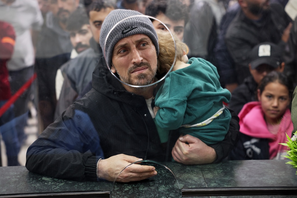 A Syrian man carries a child as they cross the Syrian-Lebanese border into Syria, fleeing Lebanon due to Israeli airstrikes, in Jdeidet Yabous, Syria, Tuesday, March 3, 2026. (AP Photo/Ghaith Alsayed)