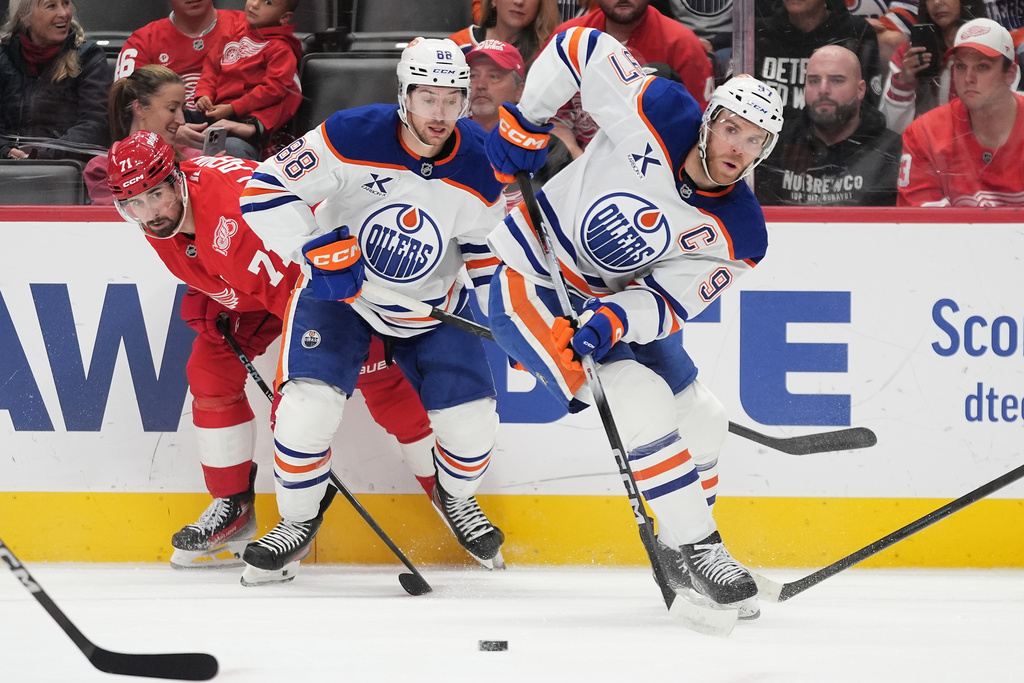 Edmonton Oilers center Connor McDavid, right, moves the puck past Oilers left wing Andrew Mangiapane, center, and Detroit Red Wings center Dylan Larkin, left, during the first period of an NHL hockey game Sunday, Oct. 19, 2025, in Detroit. (AP Photo/Ryan Sun)