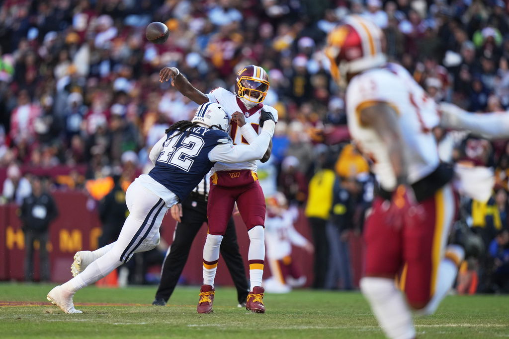 Washington Commanders quarterback Josh Johnson (14) is hit as he throws by Dallas Cowboys defensive end Jadeveon Clowney (42) during the second half an NFL football game Thursday, Dec. 25, 2025, in Landover, Md. (AP Photo/Stephanie Scarbrough)