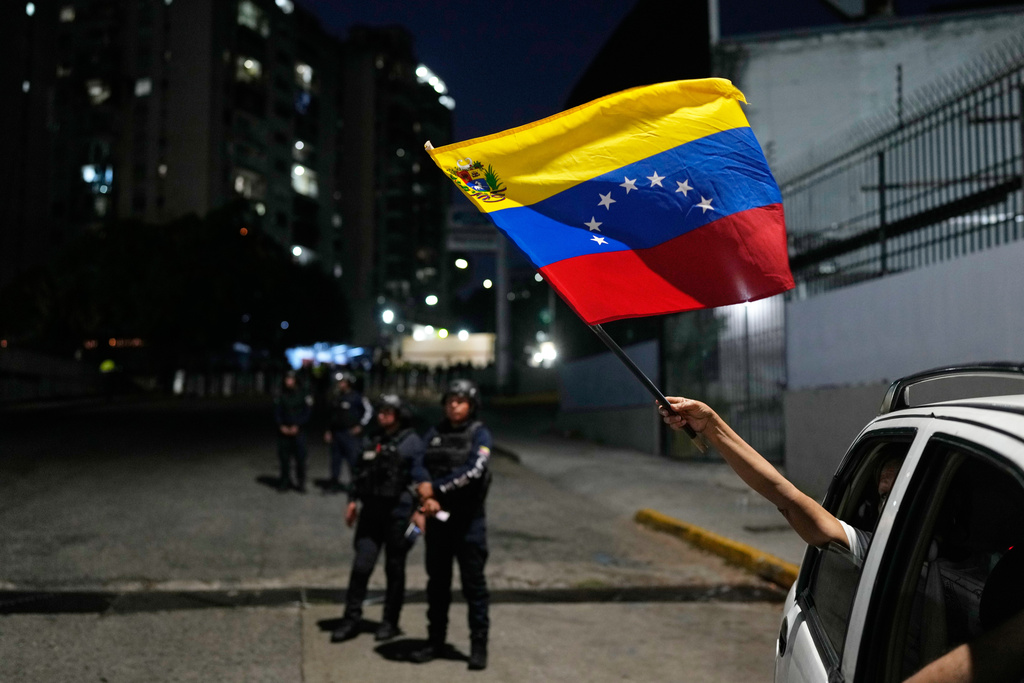 A supporter of the opposition waves a Venezuelan flag from a passing vehicle next to El Helicoide, the headquarters of the intelligence service and a detention center, after several political prisoners were released from custody in Caracas, Venezuela, Sunday, Feb. 8, 2026. (AP Photo/Ariana Cubillos)