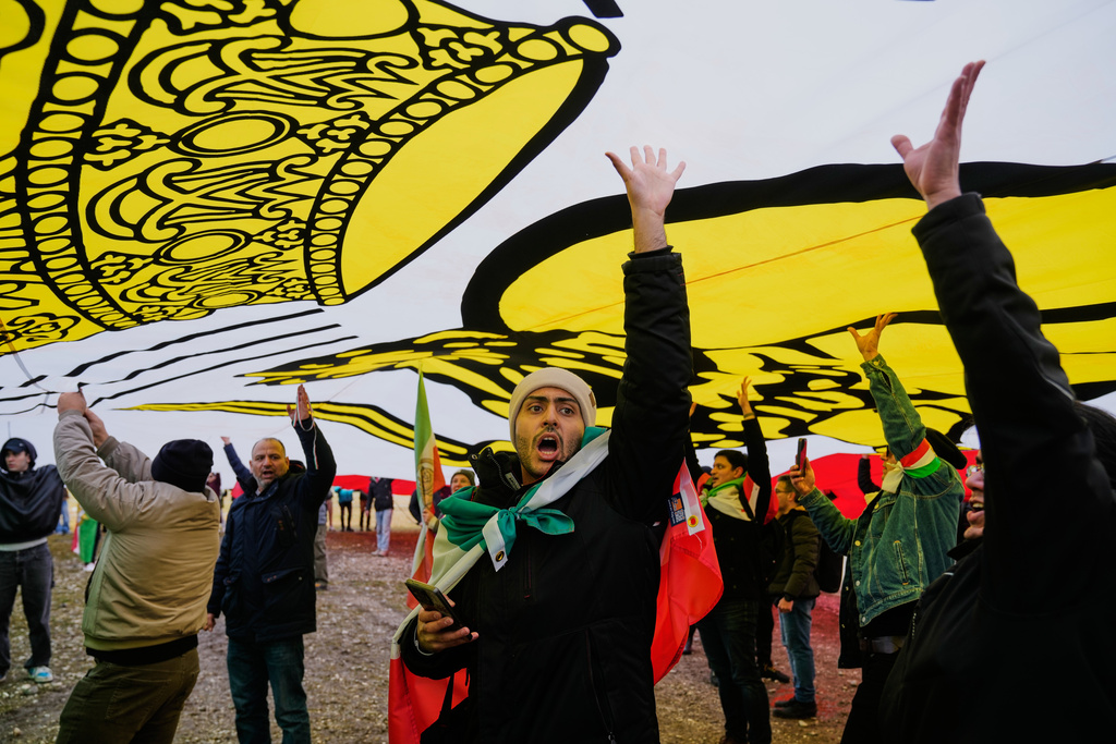 Supports of Iran's exiled Crown Prince Reza Pahlavi stand under a huge historic Iranian flag as they attend a demonstration during the Munich Security Conference in Munich, Germany, Saturday, Feb. 14, 2026. (AP Photo/Ebrahim Noroozi)