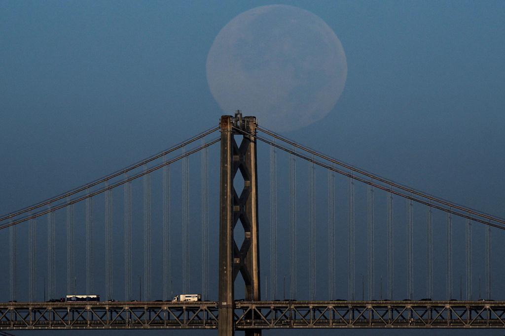 The Harvest Supermoon descends behind the Bay Bridge as seen from Alameda, Calif., Tuesday, Oct. 7, 2025. (AP Photo/Godofredo A. Vásquez)