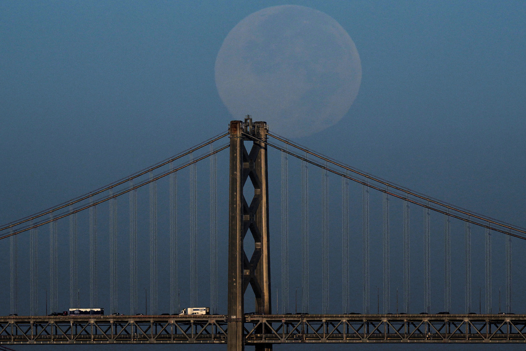 The Harvest Supermoon descends behind the Bay Bridge as seen from Alameda, Calif., Tuesday, Oct. 7, 2025. (AP Photo/Godofredo A. Vásquez)