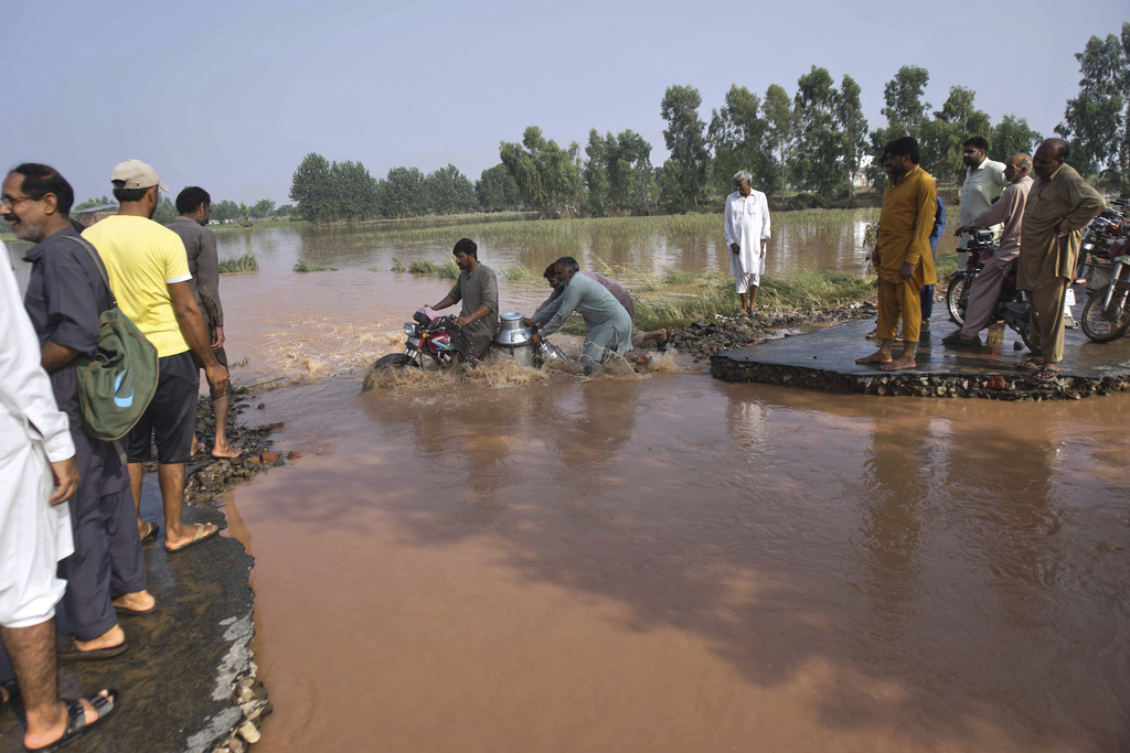 Villagers help a milkman crossing the flooded portion of a road damaged by floods after torrential rains on the outskirts of Sodhra town, in Wazirabad district, Pakistan, Friday, Aug. 29, 2025. (AP Photo/A. Rizvi)
