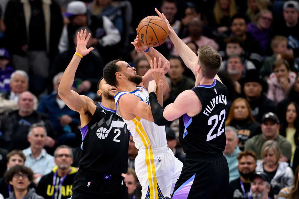 Golden State Warriors guard Stephen Curry, center, has the ball knocked away by Utah Jazz forward Kyle Filipowski, right, as he was driving to the basket during the first half of an NBA basketball game, Wednesday, Jan. 28, 2026, in Salt Lake City. (AP Photo/Tyler Tate)