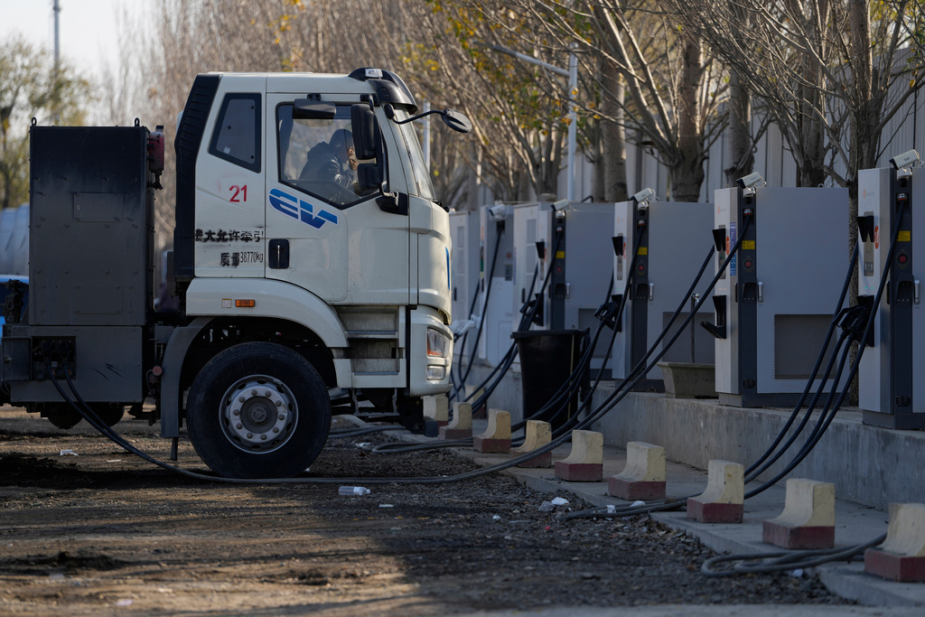 A driver rests in the cabin as his electric truck is plugged into a charging station on the outskirts of Beijing, on Nov. 14, 2025. (AP Photo/Ng Han Guan)