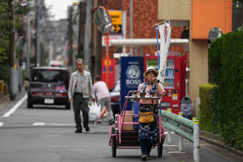 Akiko Sugaya blows an old-style horn while she peddles tofu, prepared food and beverages in a cart in Tokyo, Saturday, July 4, 2026. (AP Photo/Hiro Komae)