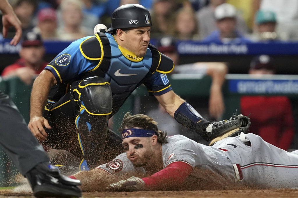 Washington Nationals' Dylan Crews, bottom, scores past Philadelphia Phillies catcher J.T. Realmuto on a single by Daylen Lile during the ninth inning of a baseball game Friday, Aug. 22, 2025, in Philadelphia. (AP Photo/Matt Slocum)