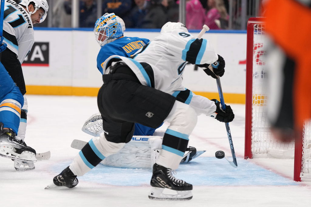 Utah Mammoth's Logan Cooley, right, scores past St. Louis Blues goaltender Jordan Binnington, left, for his third goal of the first period of an NHL hockey game Thursday, Oct. 23, 2025, in St. Louis. (AP Photo/Jeff Roberson)