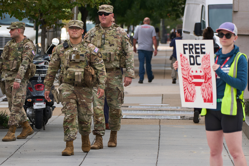 As members of the National Guard walk on patrol, protesters from Free DC rally against continued National Guard presence in the district, on the one year anniversary of President Trump's emergency declaration activating the National Guard, Tuesday, Aug. 11, 2026, in Washington. (AP Photo/Jacquelyn Martin)