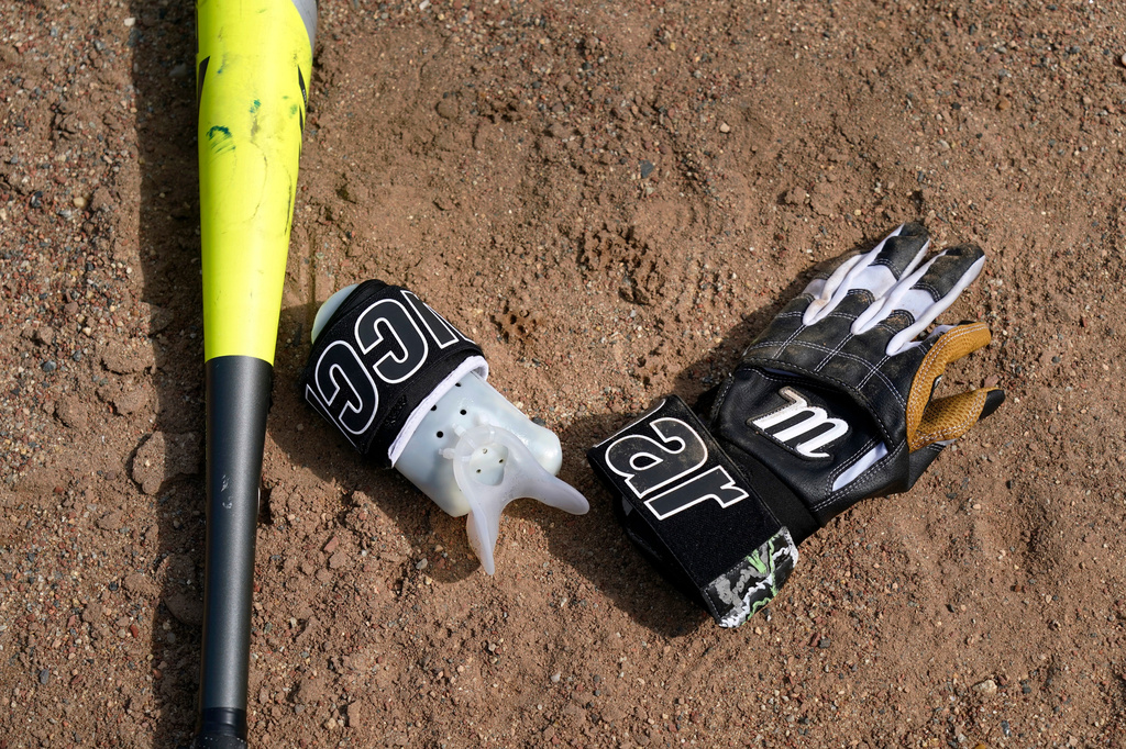 A bat, glove and a device to allow Brittany Apgar, who was born without a right hand, to hold a bat are shown at a field in Greensboro, N.C., Wednesday, July 22, 2026. (AP Photo/Chuck Burton)