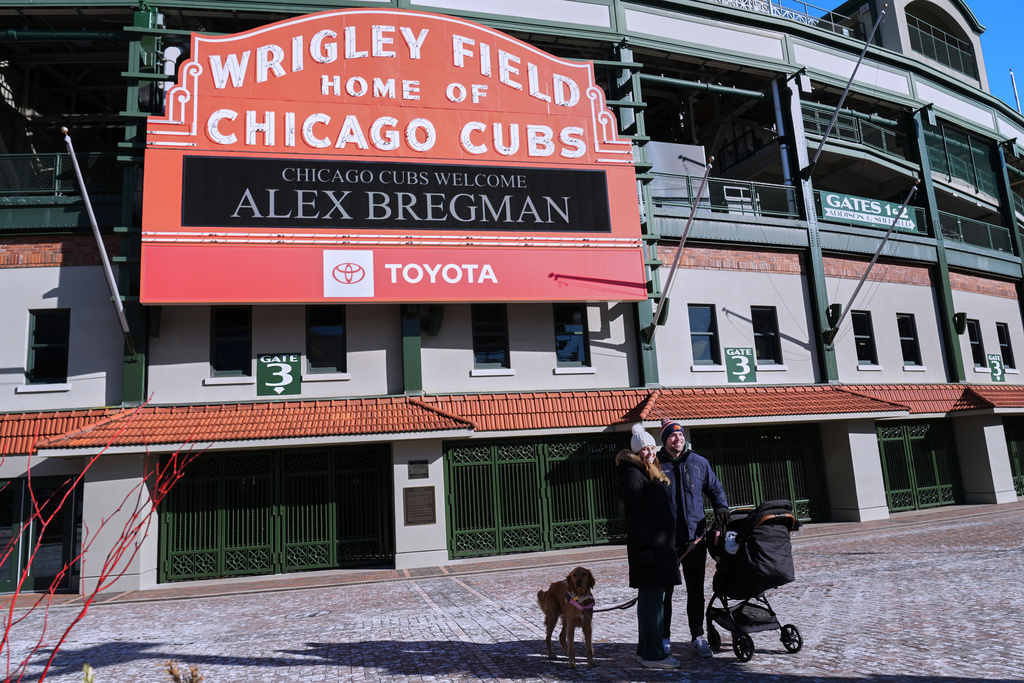 Catrina Connelly, left, her husband Patrick Connelly, their baby Declan with their dog Millie stand outside of Wrigley Field where the marquee displays new Chicago Cubs infielder Alex Bregman, Thursday, Jan. 15, 2026. (AP Photo/Nam Y. Huh)