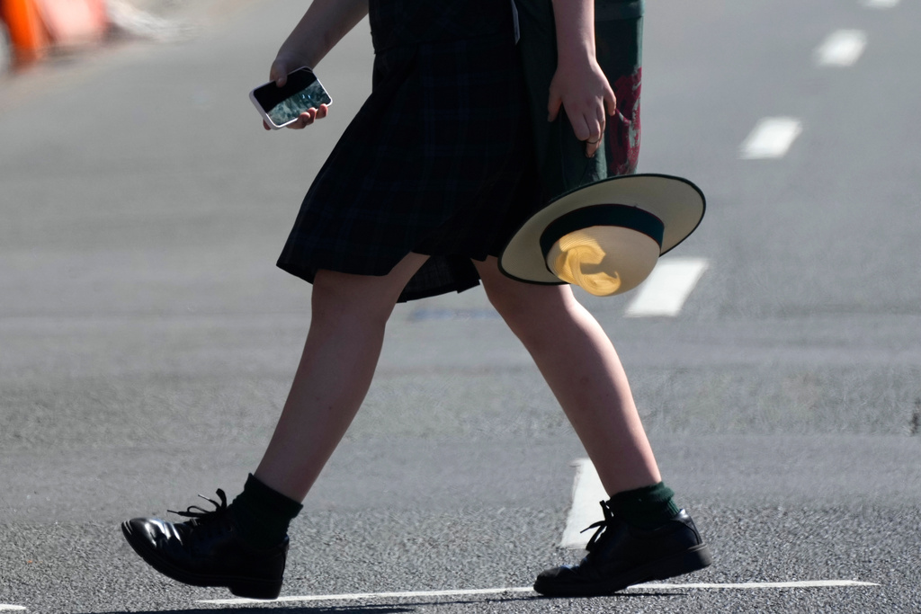 FILE - A school girl holds her phone while crossing a street in Sydney, on Nov. 8, 2024. (AP Photo/Rick Rycroft, File)
